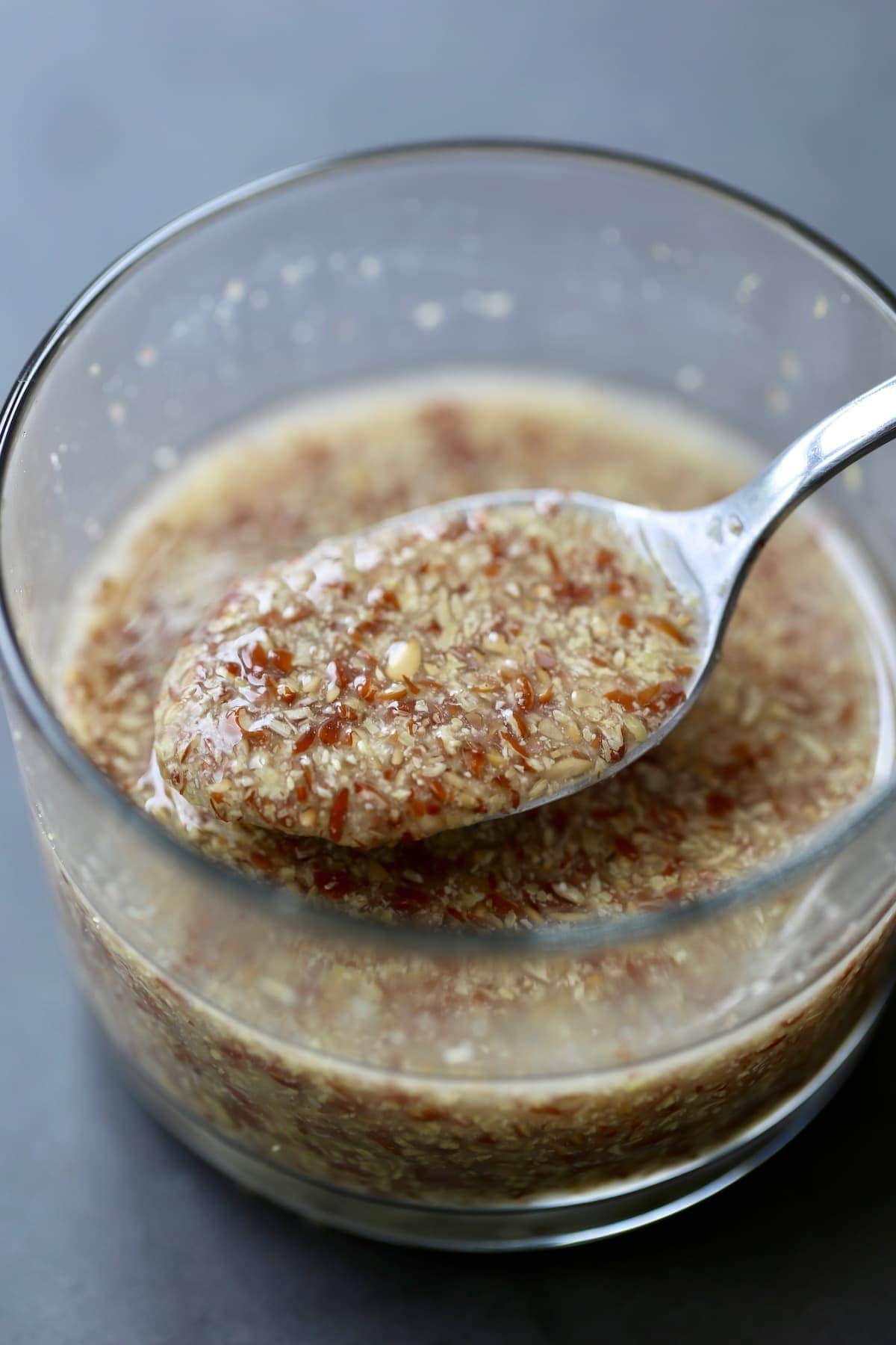 A metal spoon scooping up a flaxseed and water mixture in a clear bowl.