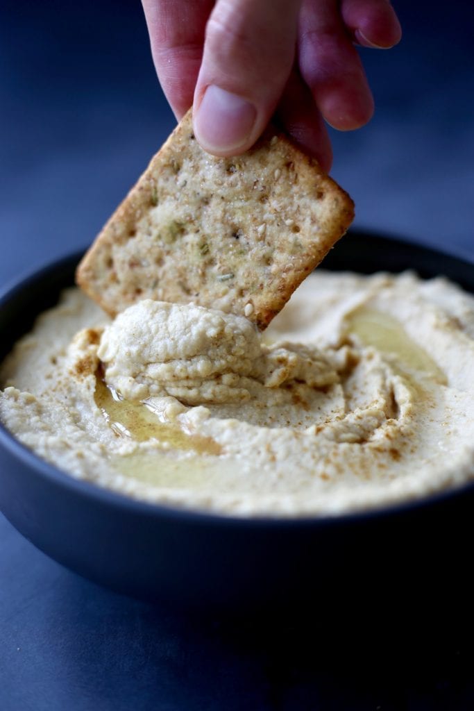 Hummus being scooped up with a cracker
