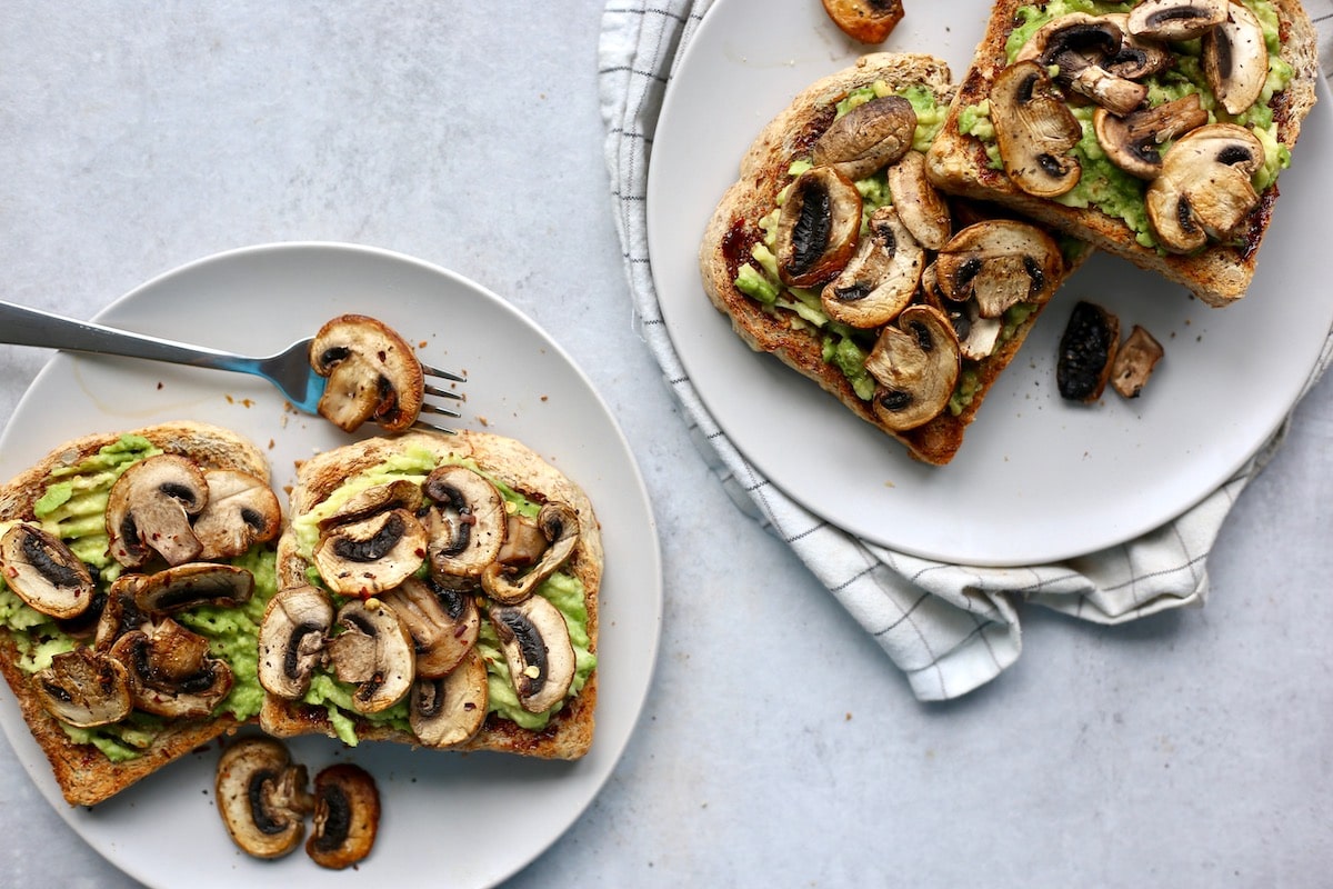 Two plates loaded with marmite avocado toast and sauteed mushrooms