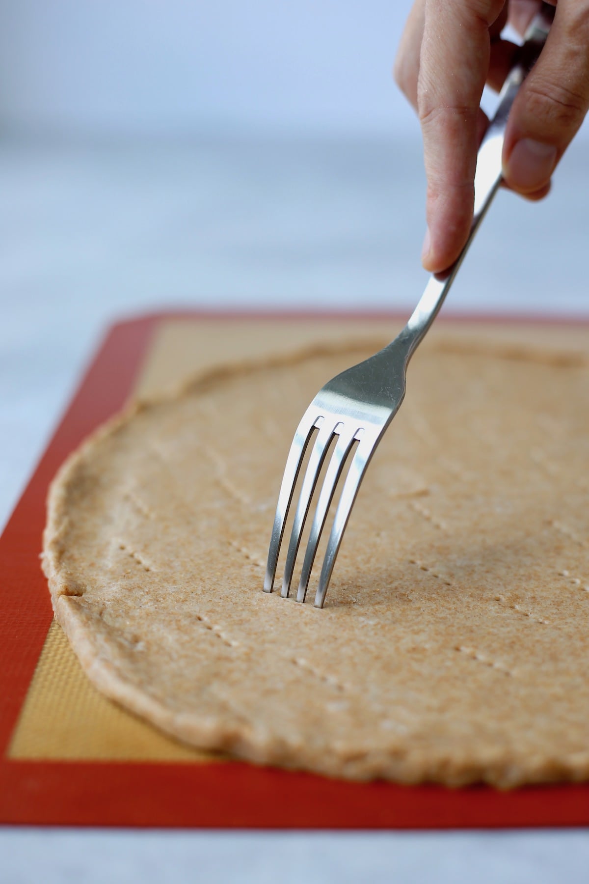 A hand poking holes into a whole wheat pizza crust using a fork. 