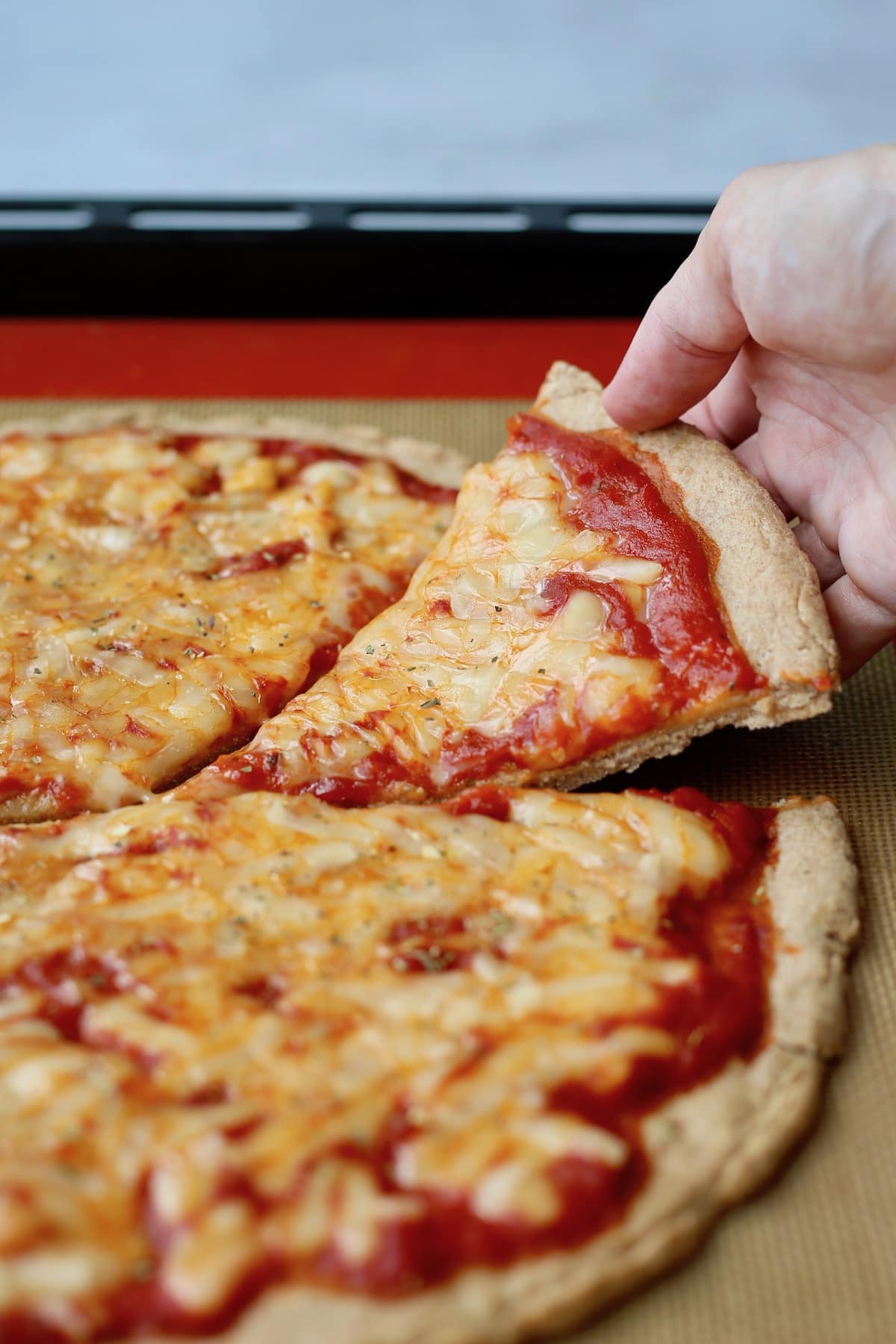 A slice of cheesy vegan cheese pizza being being taken off a baking sheet.