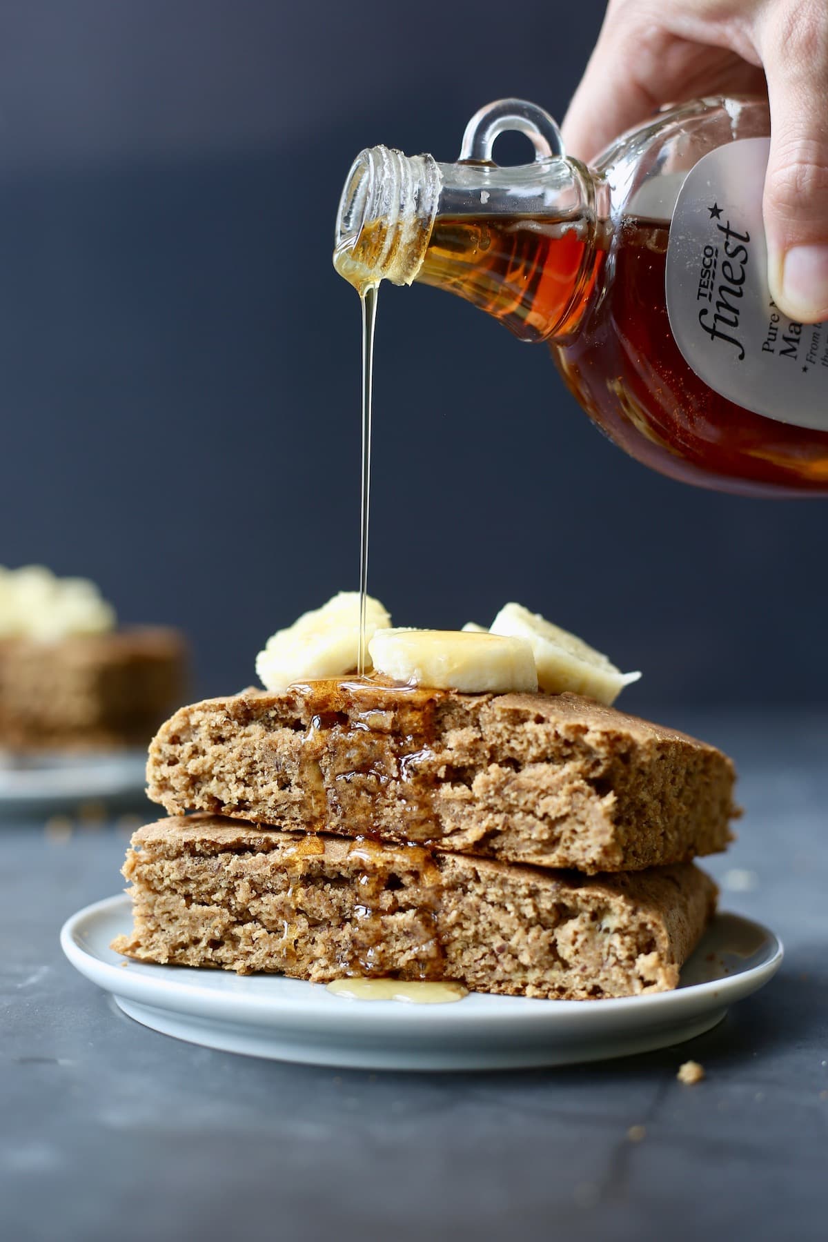 maple syrup being drizzled over a stack of super thick and fluffy vegan sheet pan pancakes