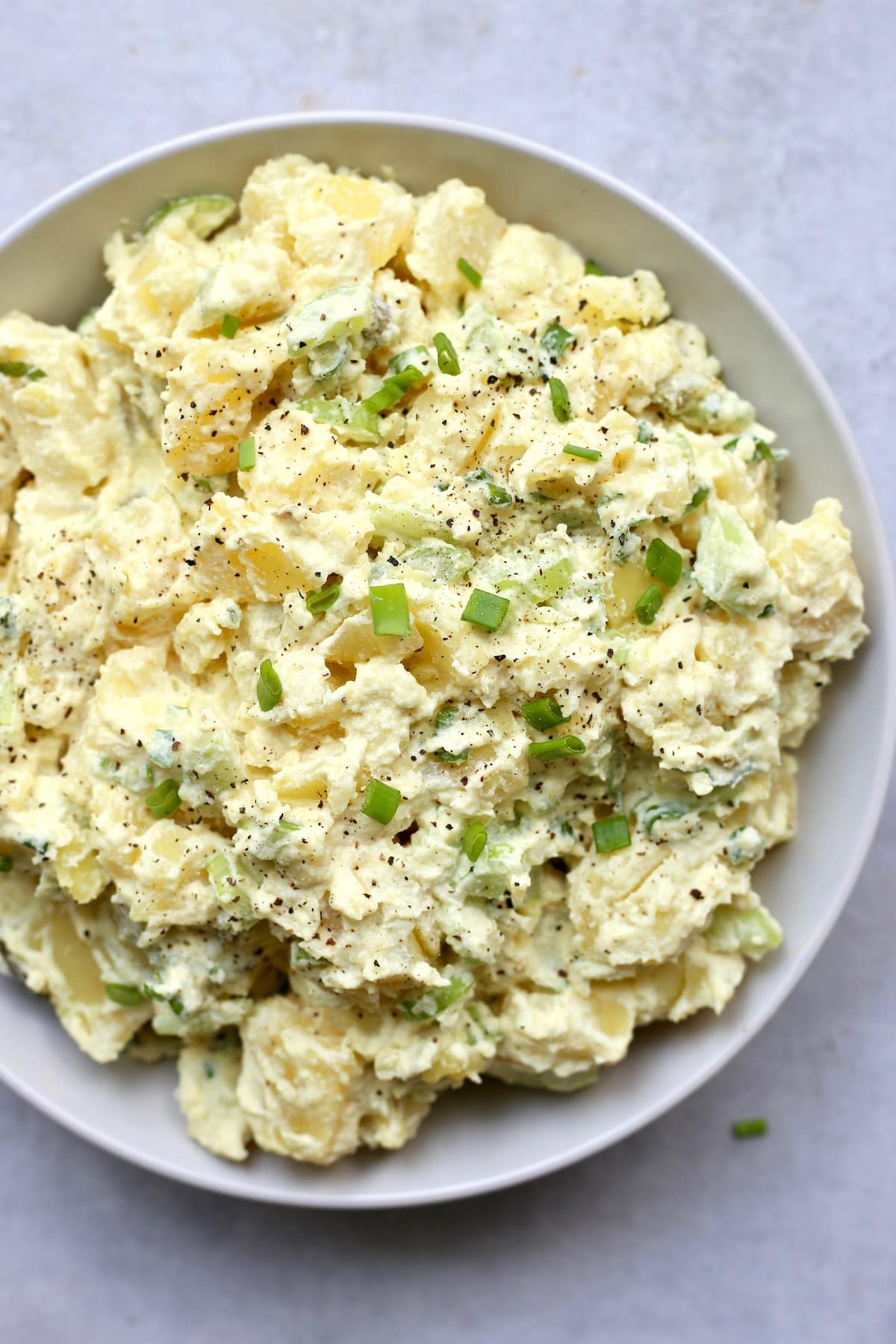 Creamy vegan potato salad in a large bowl topped with green onion and lots of black pepper