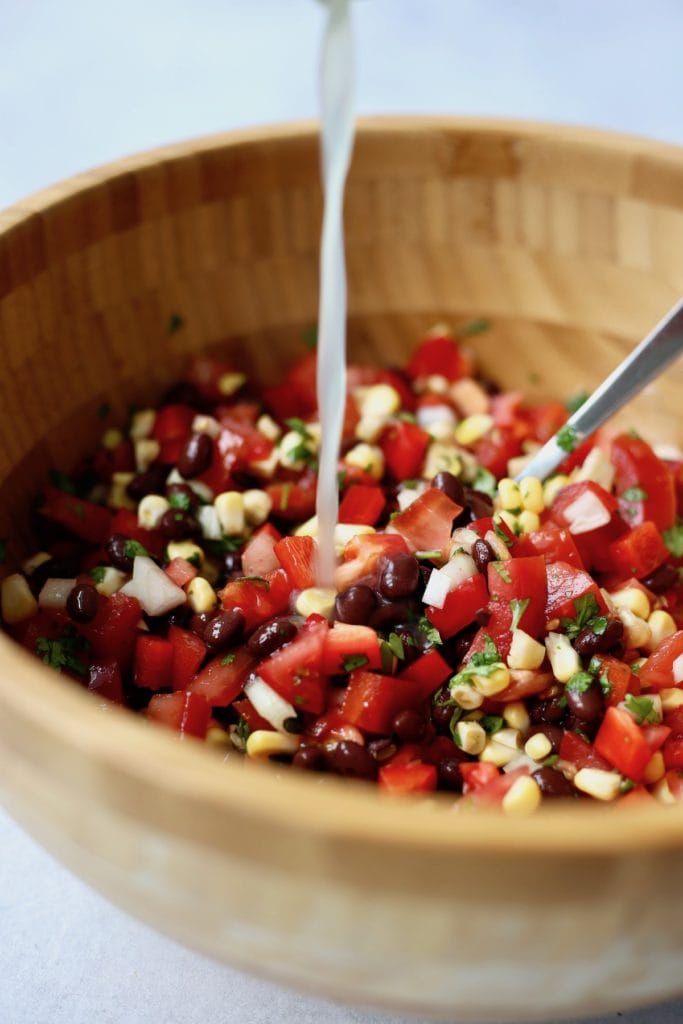 Lime juice being poured over black bean and corn salad in a bowl