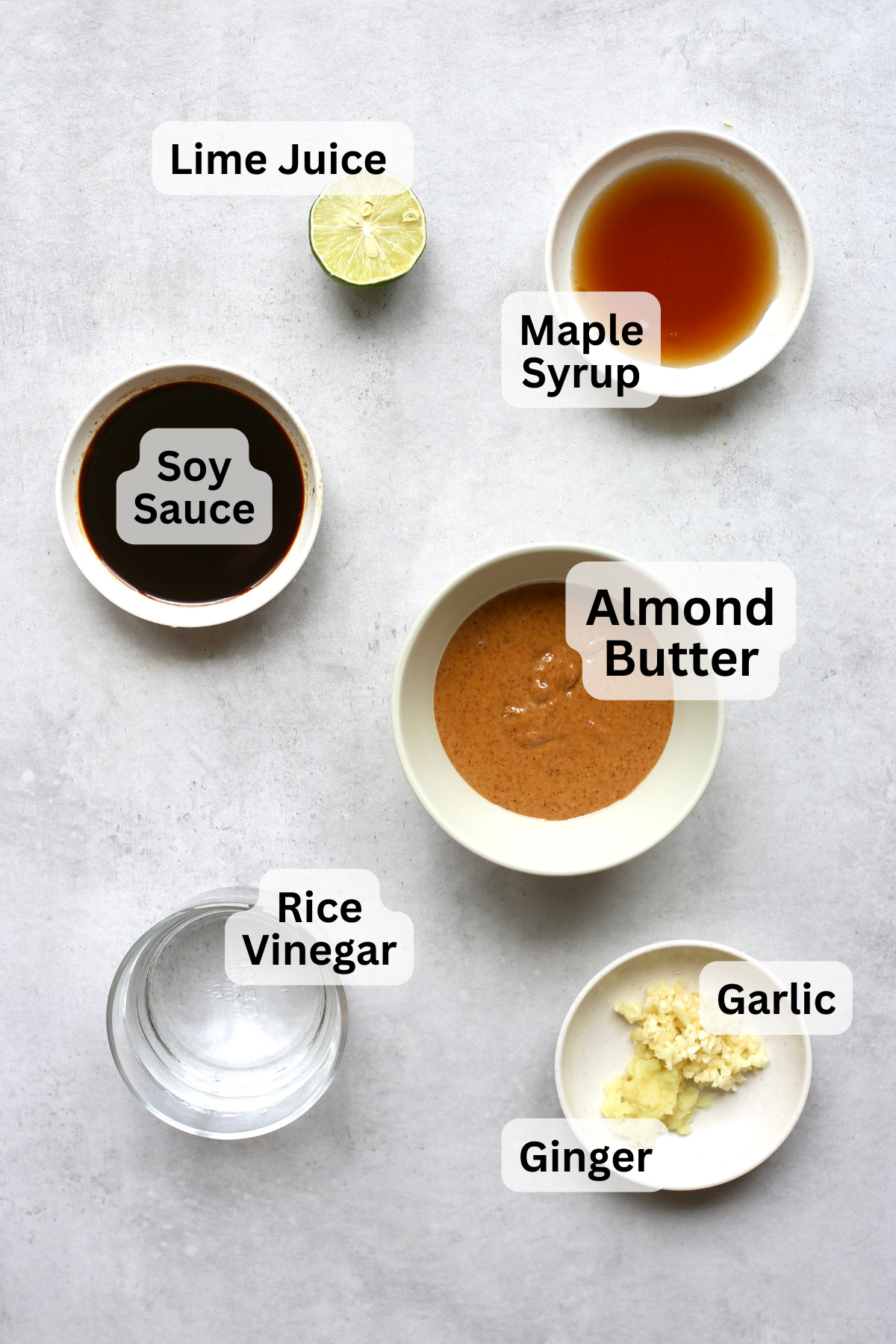 An overhead shot of the the ingredients for savory almond butter sauce measured out into small bowls with labels overtop. 