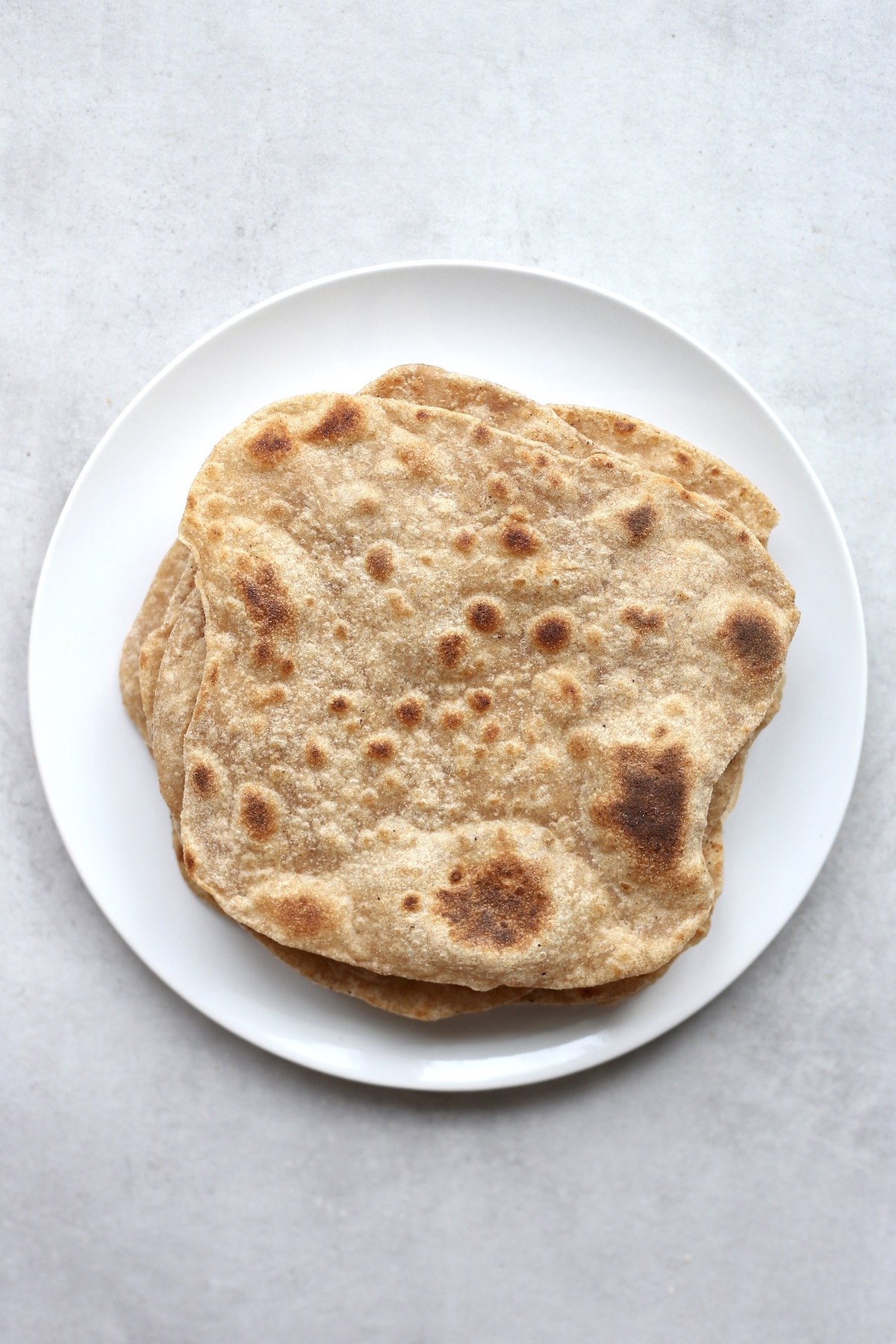 A large white plate with a stack of chapati on top of it. 