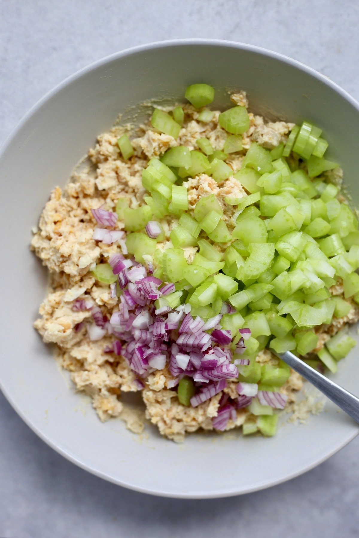 Chopped celery and red onion on top of mashed chickpeas in a bowl.