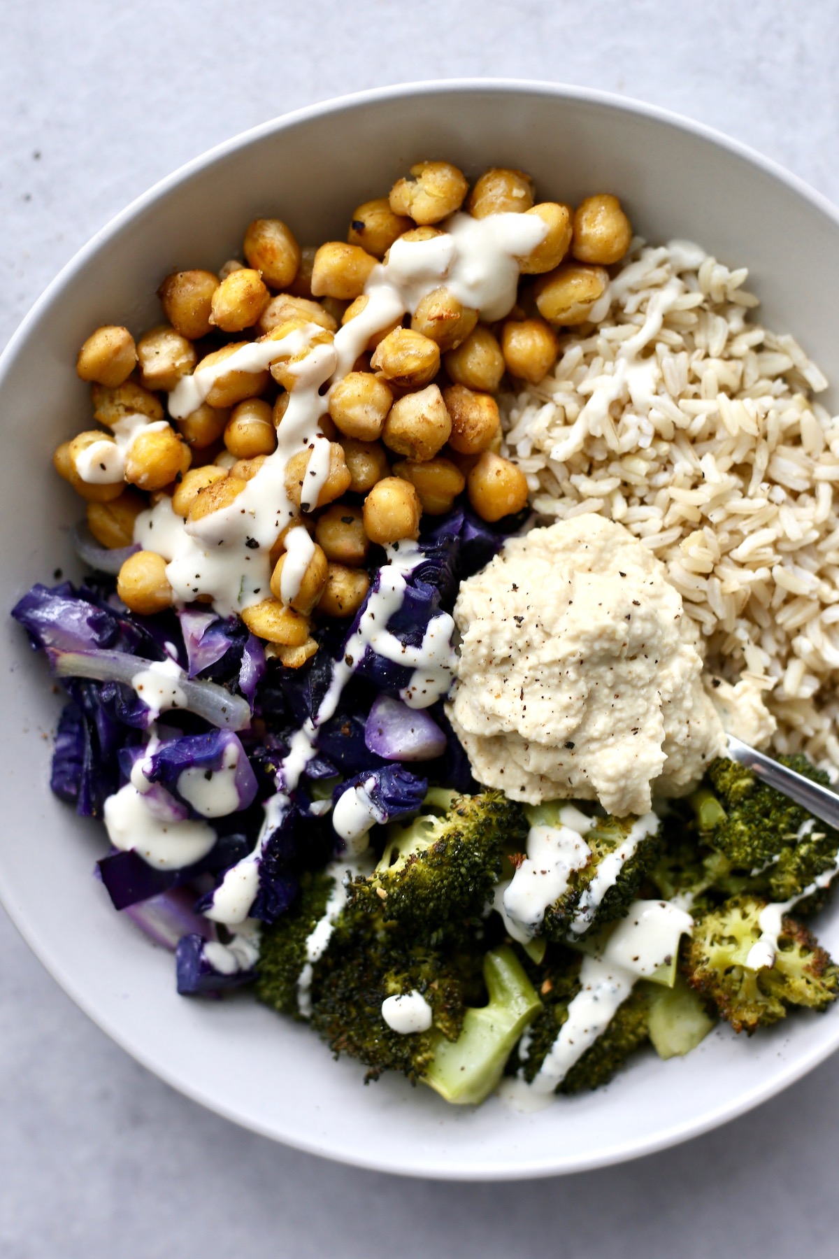 a bowl loaded with brown rice and roasted chickpeas, cabbage and broccoli, drizzled with tahini dressing