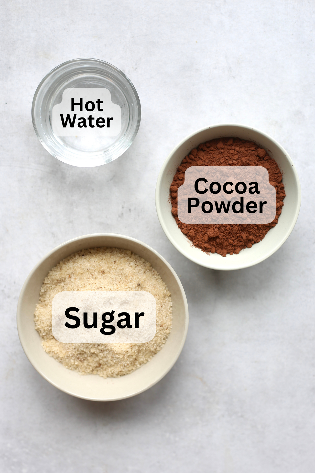 Water, cocoa powder and sugar measured out into bowls with labels over them.