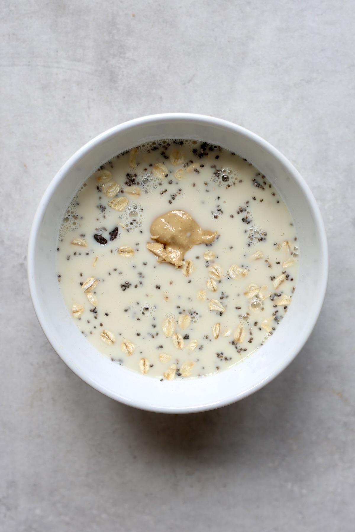 An overhead shot of milk, oats and cashew butter in a white bowl.