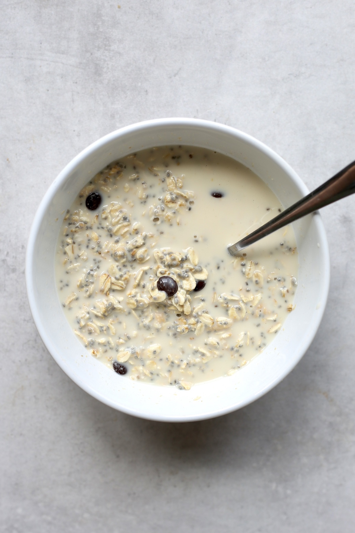 A spoon stirring together milk, oats and cashew butter in a white bowl for cookie dough overnight oats.
