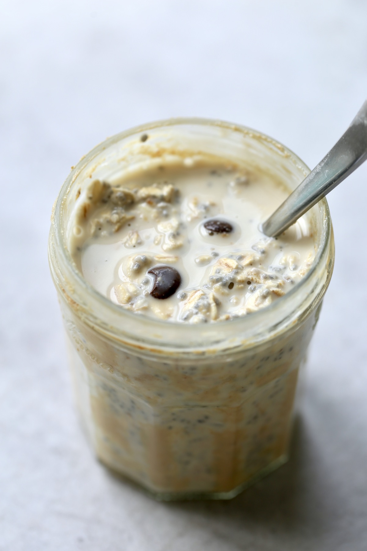 A mason jar full of rolled oats, cacao chips and milk with a spoon sticking into it. 