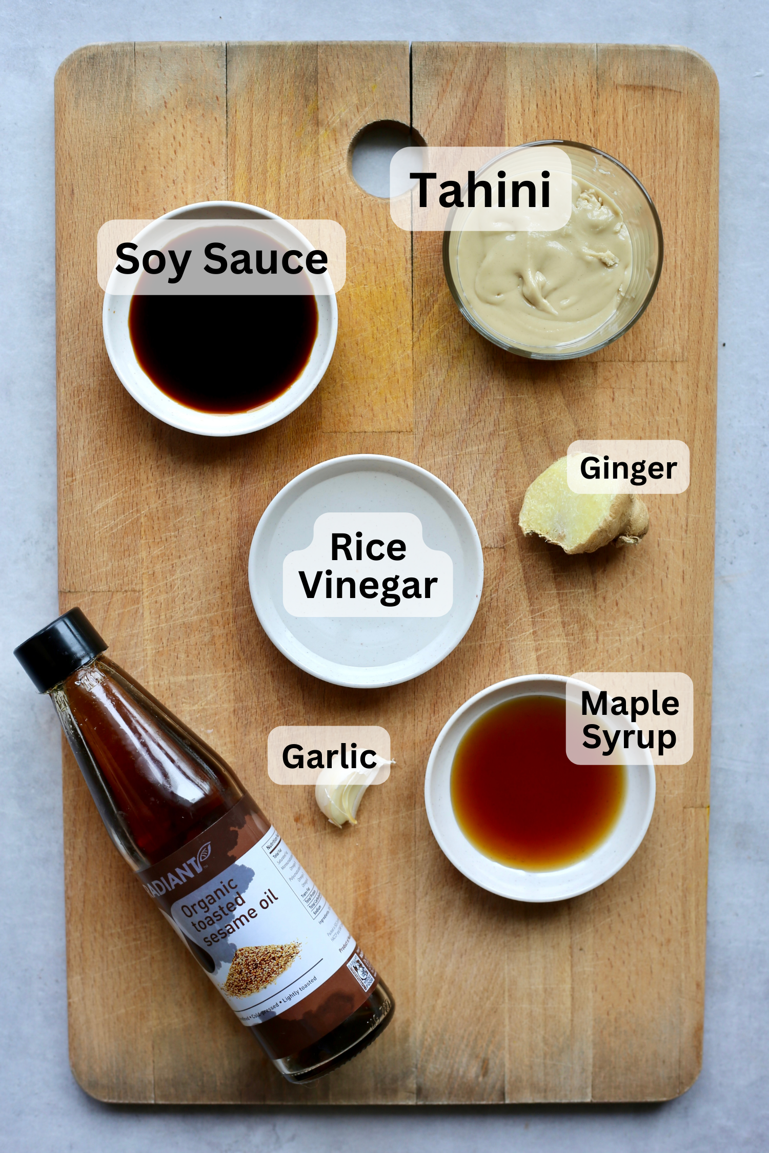 Tahini, soy sauce, rice vinegar, ginger, maple syrup, sesame oil and garlic laid out on a wooden cutting board for making crack sauce. 