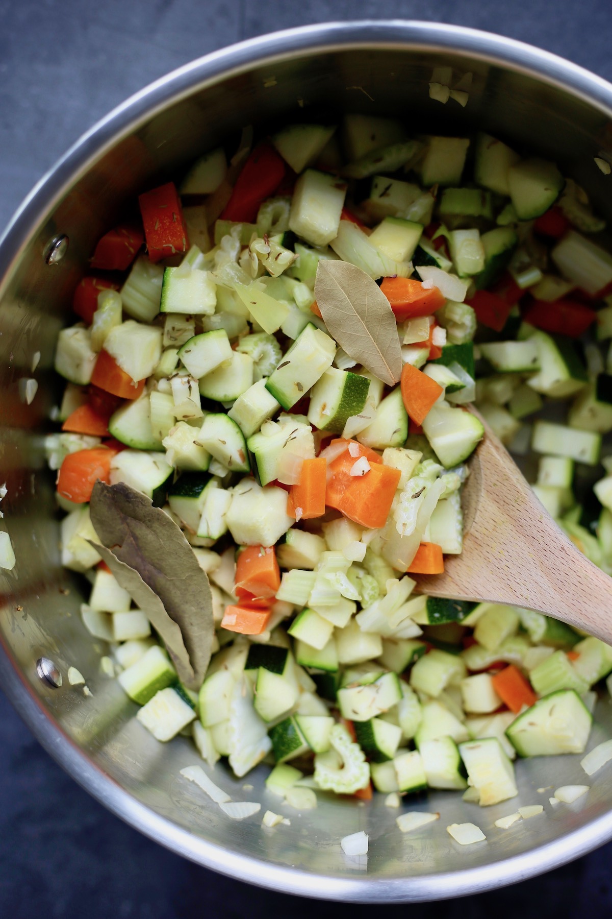 Chopped up zucchini and carrots in a silver sauce pan with bay leaves and thyme sprinkled on top.