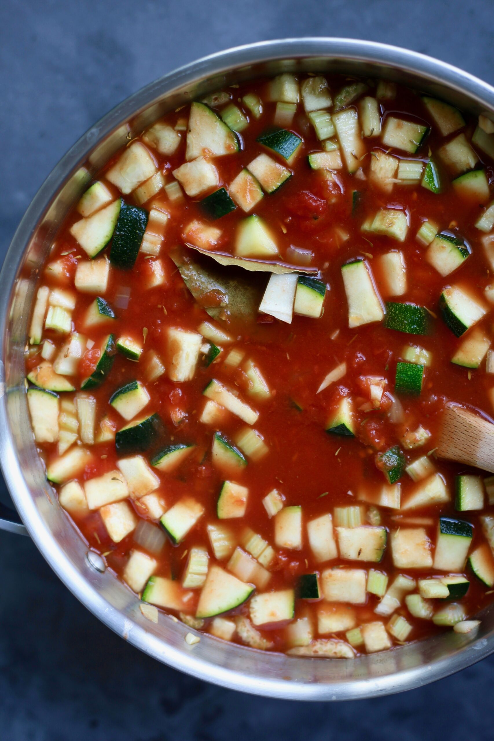 Chopped zucchini poking out of red tomato soup in a silver pot. 