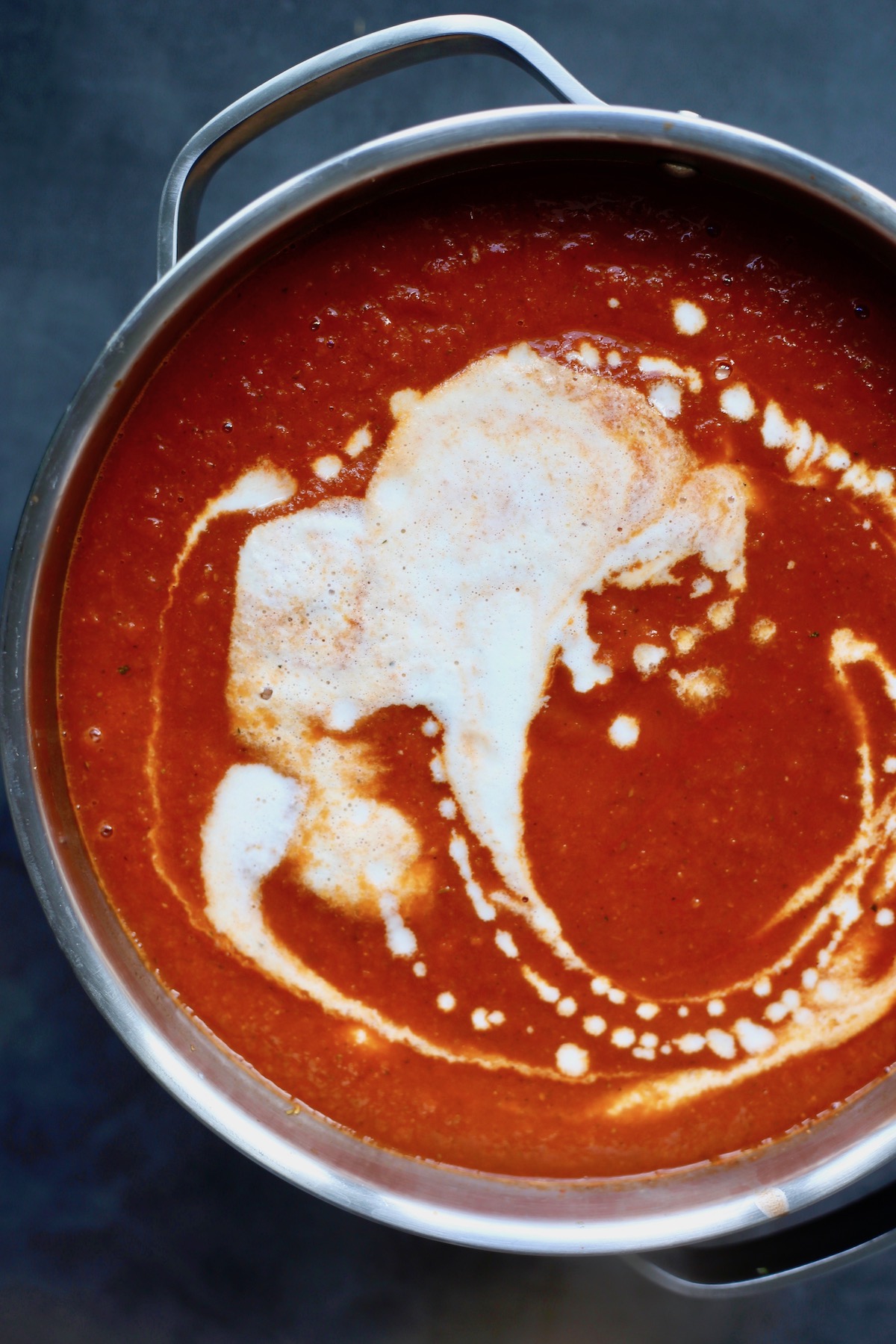 Cashew sauce drizzled into vibrant red tomato zucchini soup in a fun pattern. 