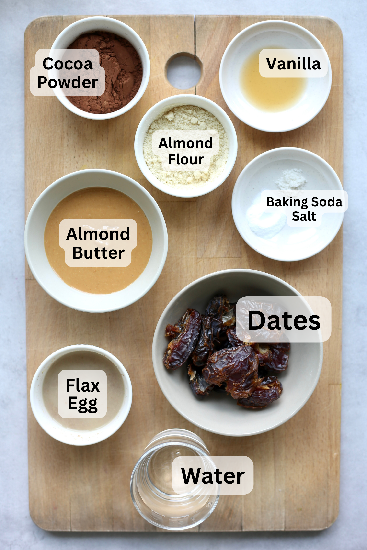 All of the ingredients for date brownies measured out into bowls on a wooden cutting board. 