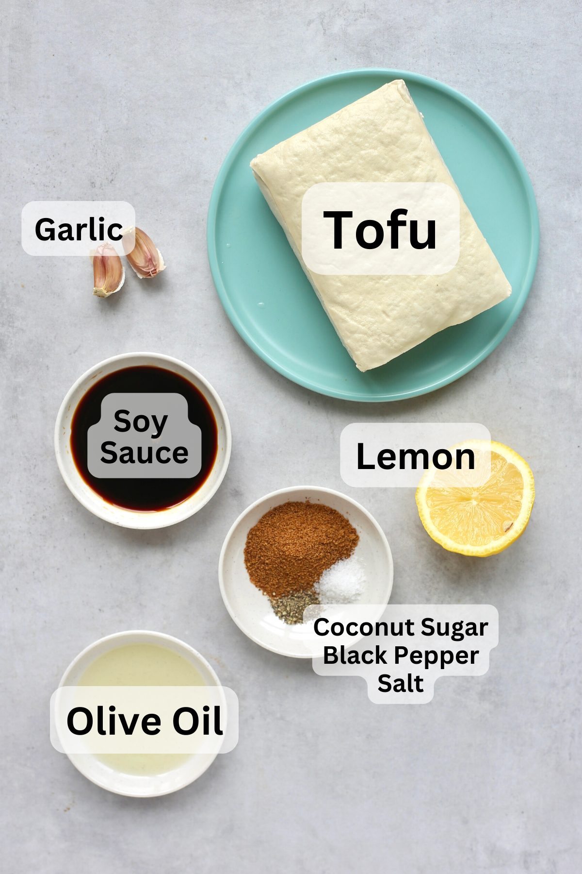 Tofu, soy sauce, spices, garlic, olive oil, and half a lemon measured out into bowls with labels overtop.