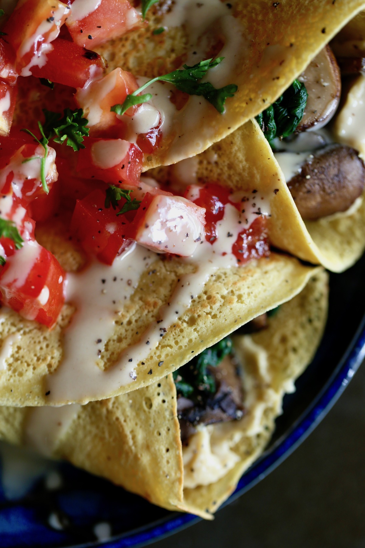 two savory chickpea flour crepes willed with hummus, sauteed mushrooms and greens and topped with runny tahini, tomatoes and parsley