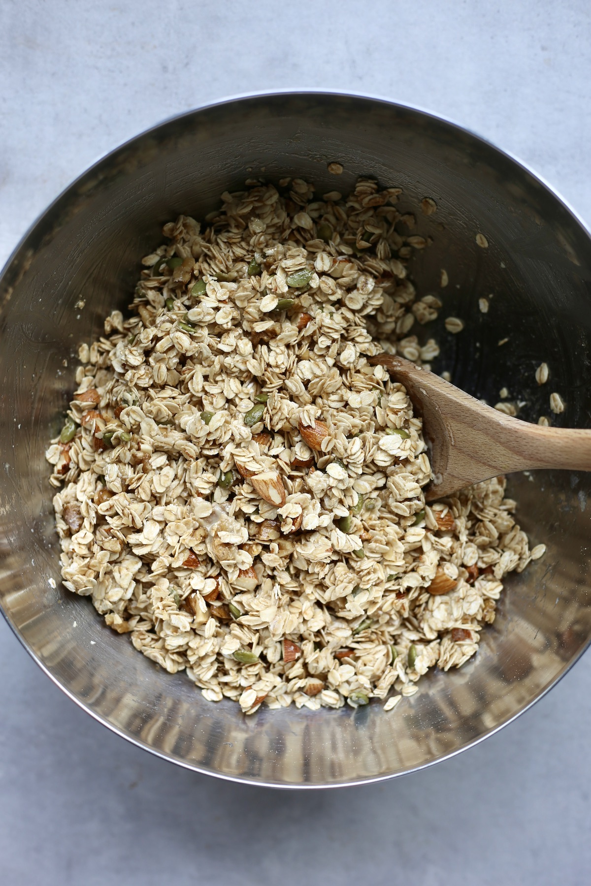 A wooden spoon stirring oats, nuts and seeds together in a mixing bowl for granola.