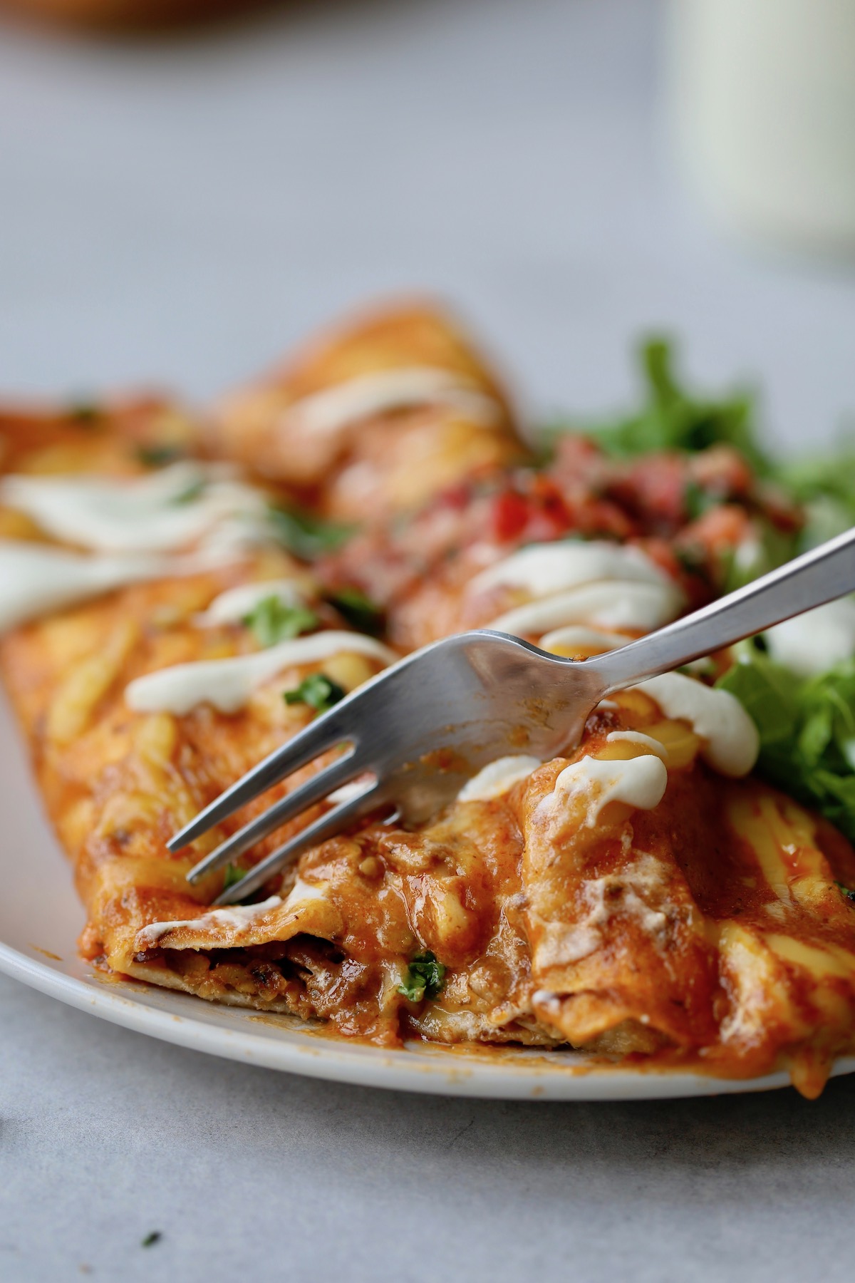 A fork cutting into cheesy vegan enchiladas.