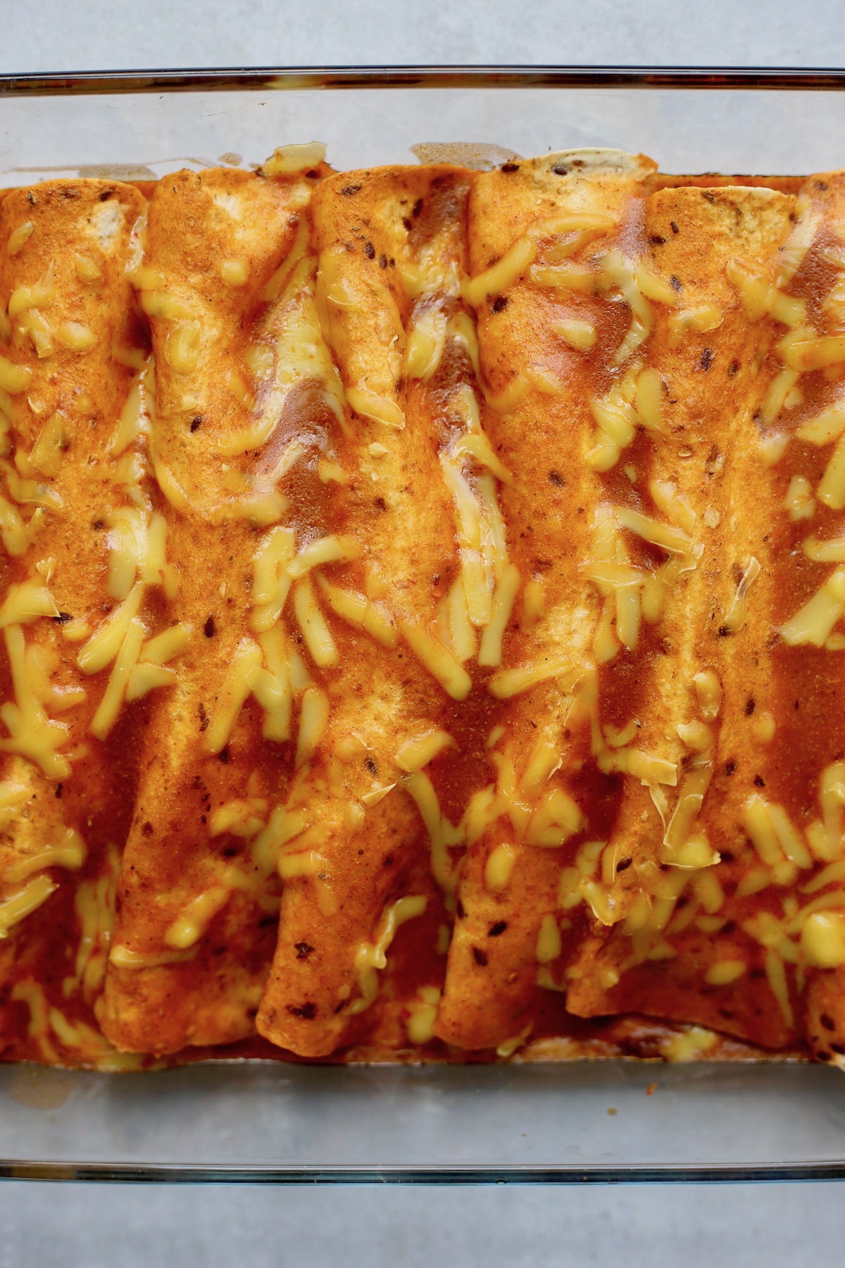 An above shot of yellow, gooey cheese melted on top of vegan enchiladas in a glass baking dish. 