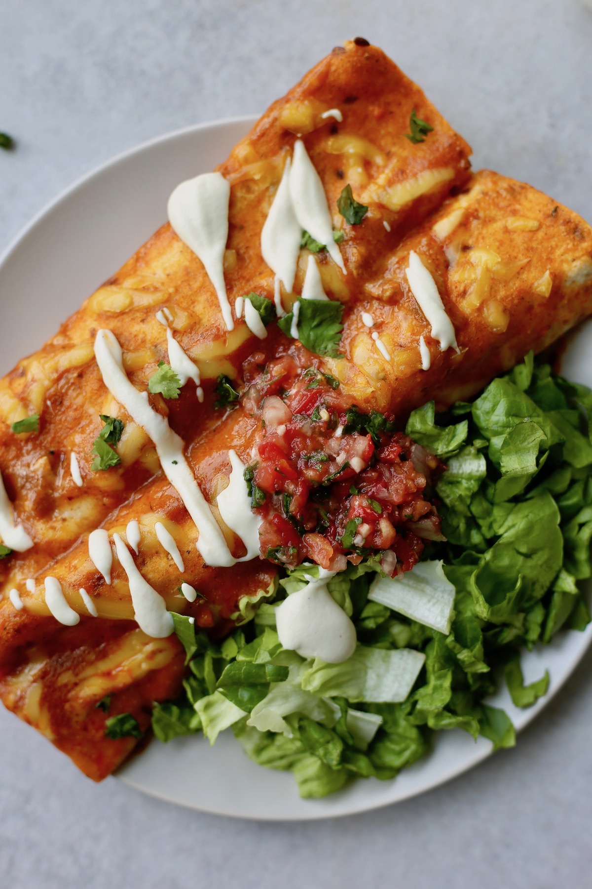 Vegan enchiladas topped with cashew sour cream, salsa and cilantro beside a pile of lettuce.