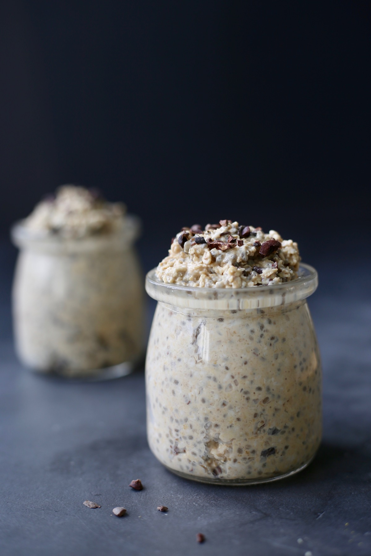Two clear little jars of vegan cookie dough overnight oats topped with cacao nibs.