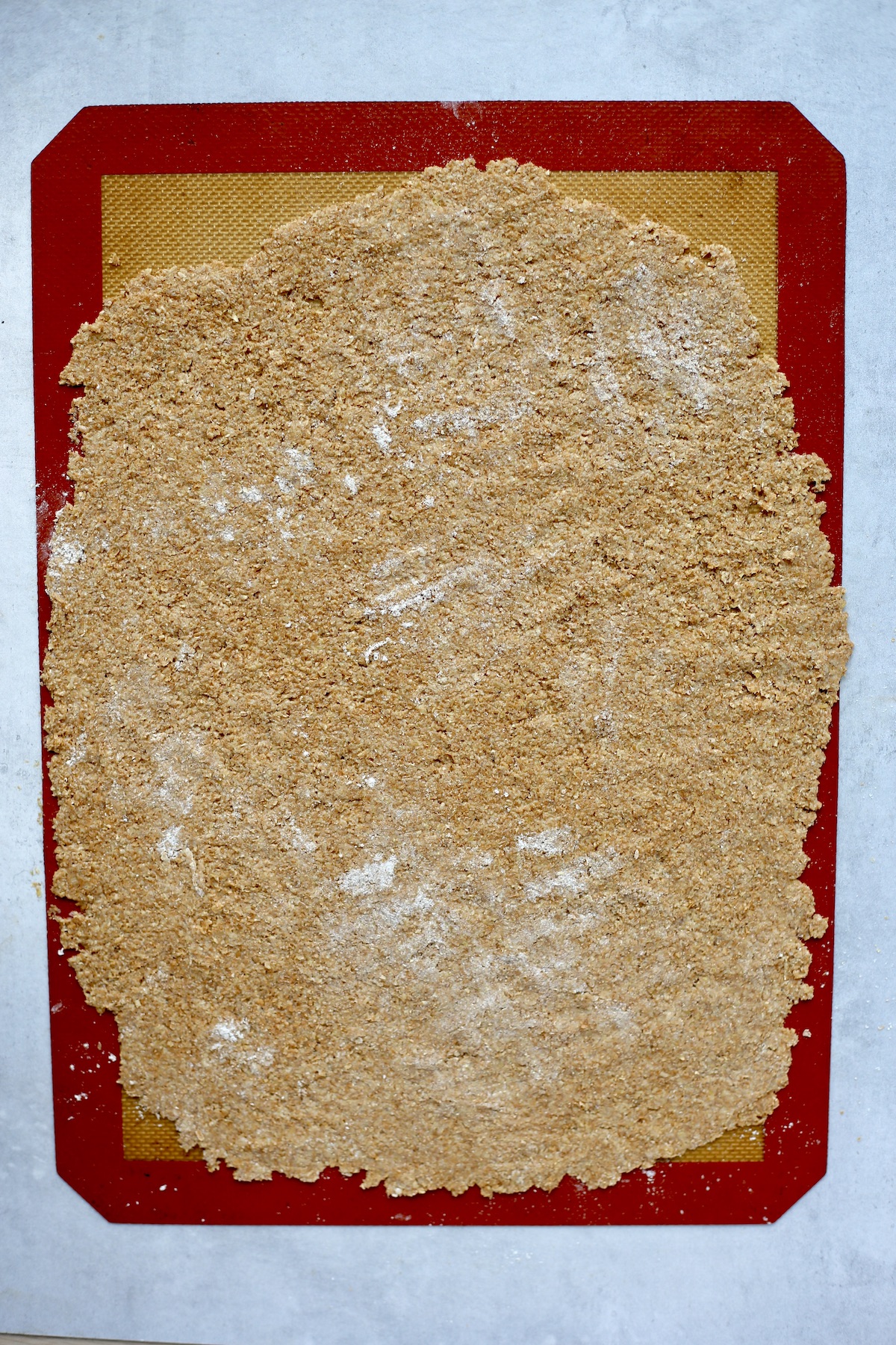 A thin sheet of whole wheat dough rolled out on a silicone baking mat with a red border. 