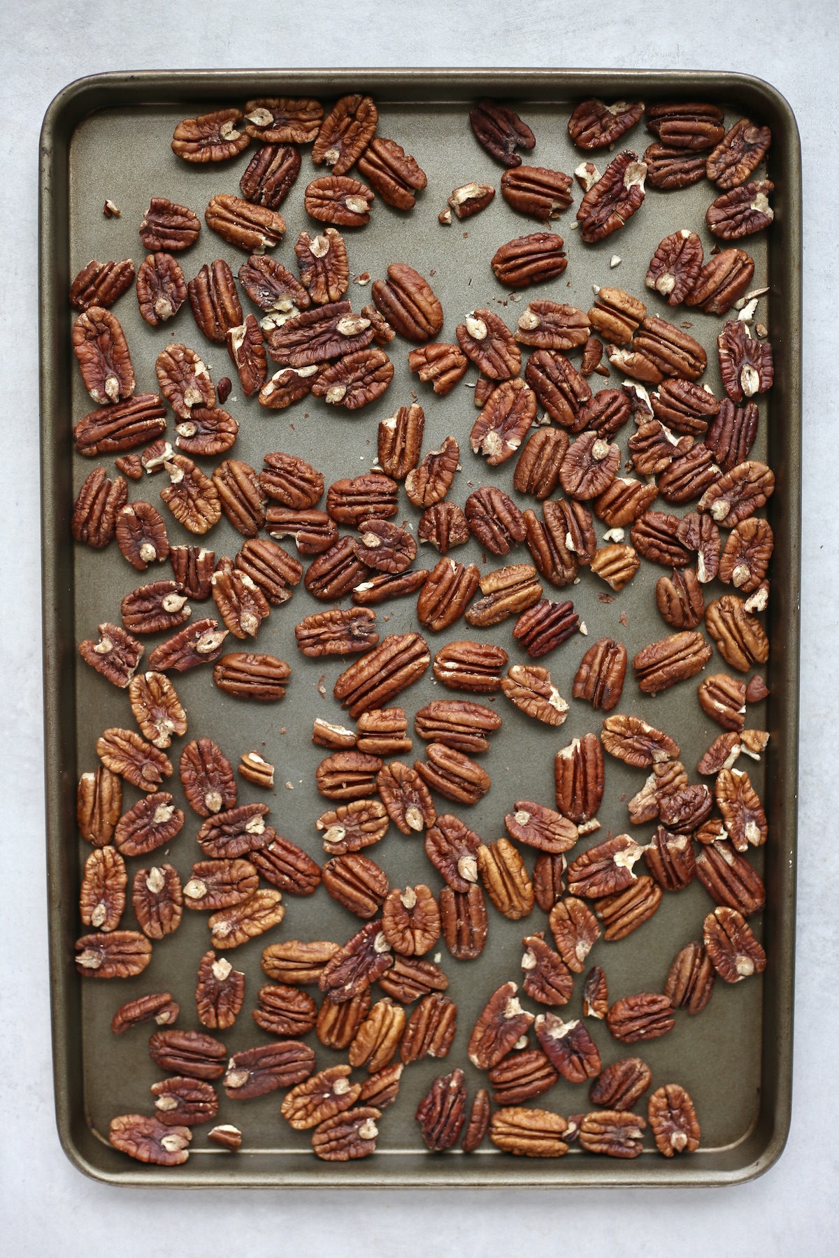 Raw pecans spread out on a silver baking sheet. 