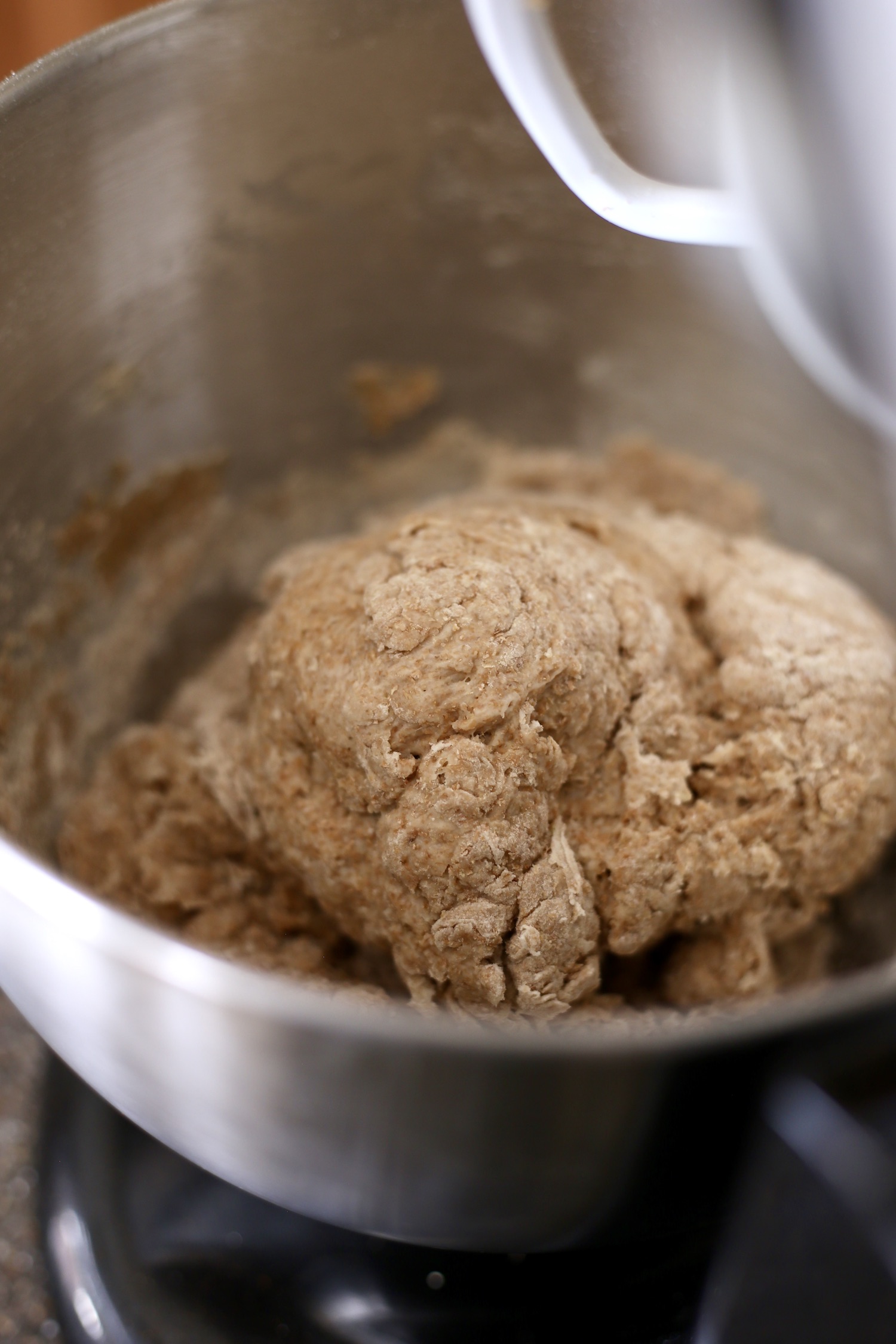 A stand mixer with a shaggy ball of whole wheat dough in the bowl.