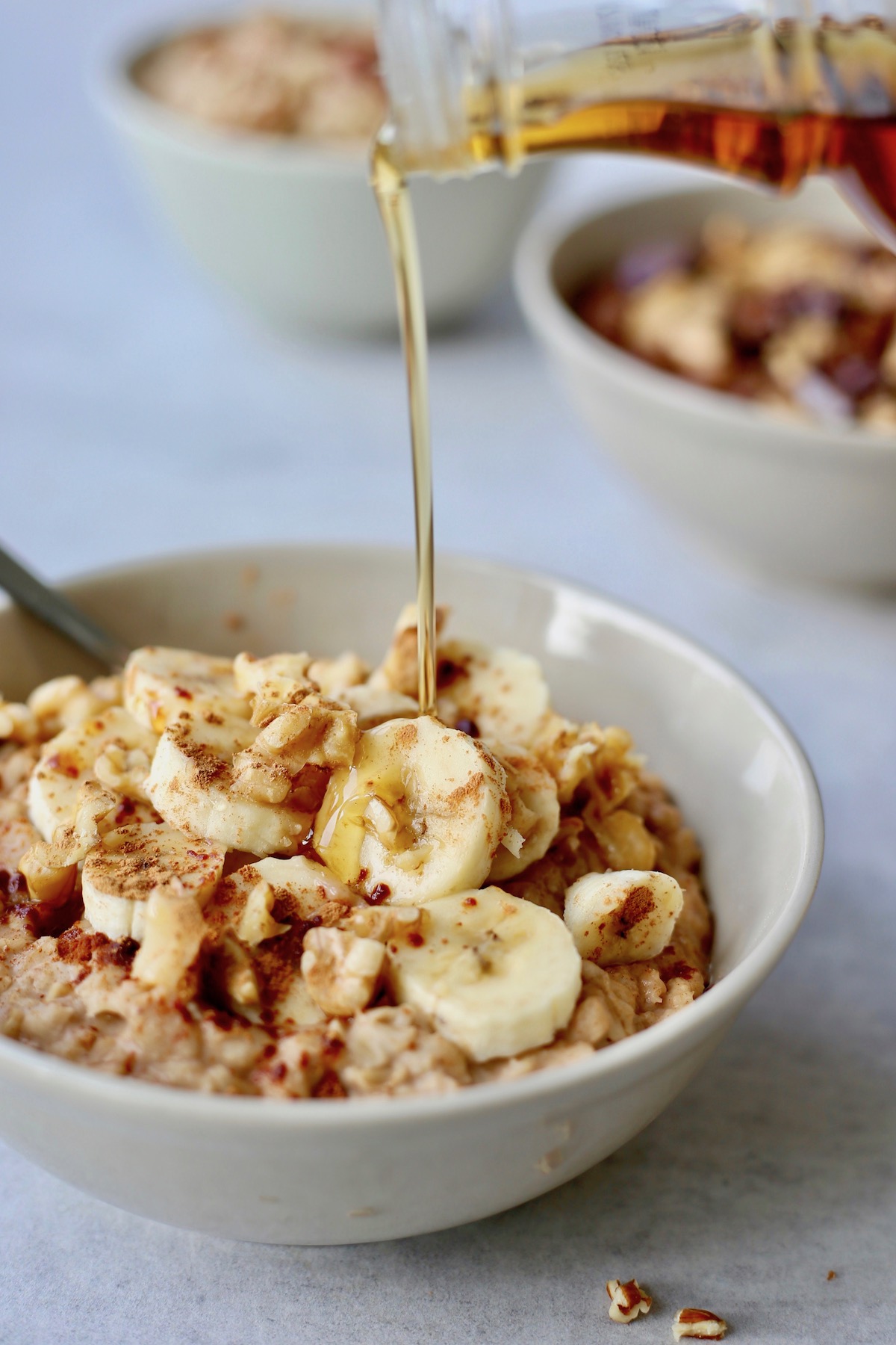 maple syrup being poured onto a bowl of banana oatmeal