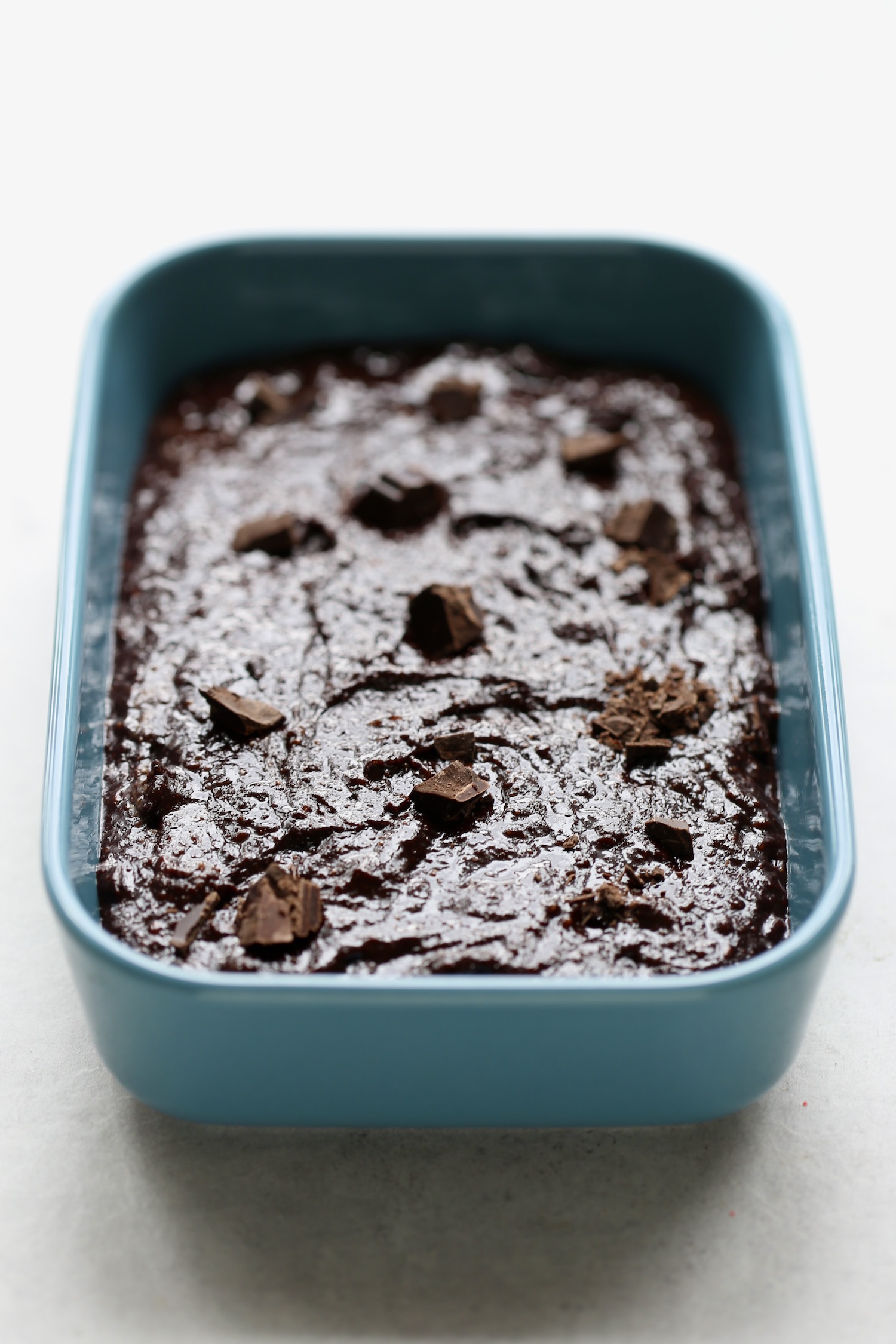 Tahini brownie batter spread out in a blue loaf pan sprinkled with more chocolate chips.