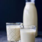 two glasses of oat milk next to a jar of oat milk