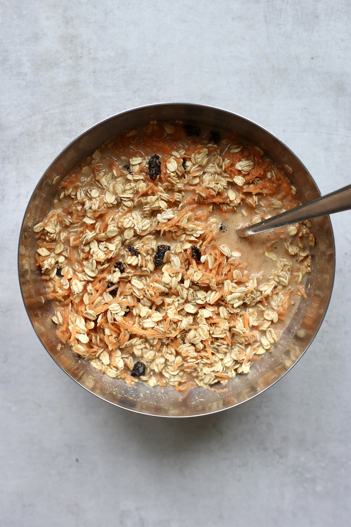 Carrot cake baked oatmeal batter being stirred together in a metal mixing bowl.