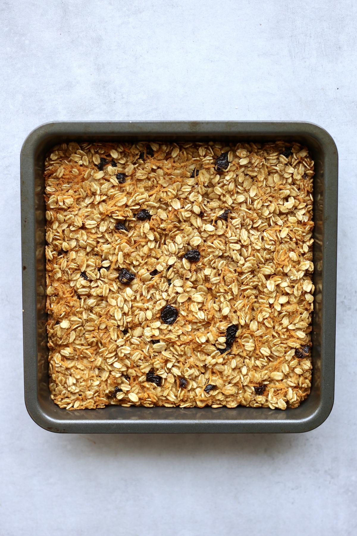 The inside of carrot cake baked oatmeal with carrots and raisin in a blue rectangle baking dish. 