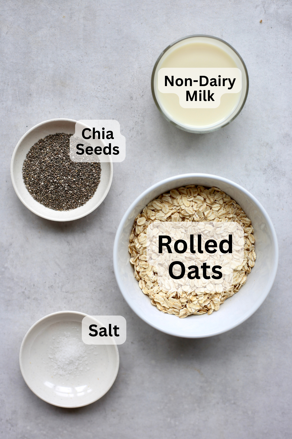 Non-dairy milk, chia seeds, rolled oats and salt measured out into bowls for vegan overnight oats. 