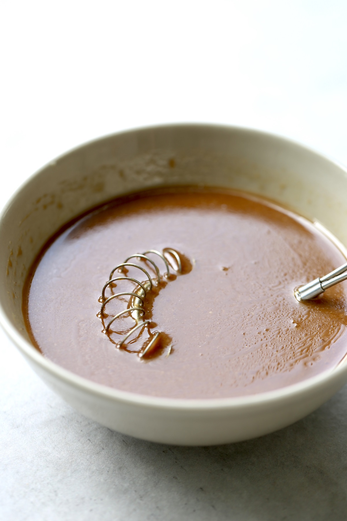 A small whisk sitting in some brown miso sauce in a small tan bowl.