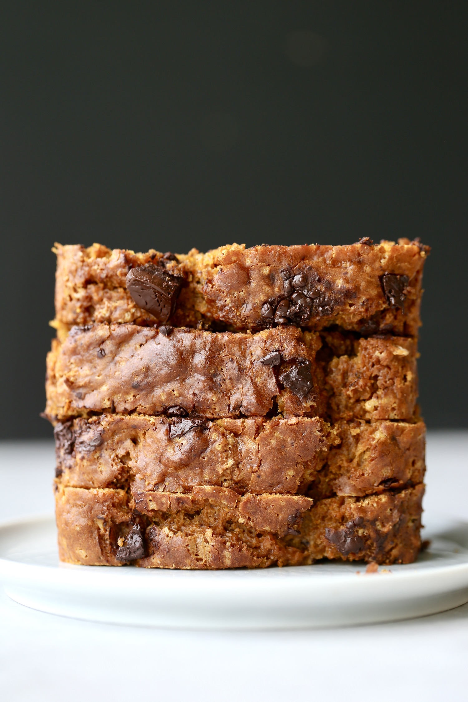 4 thick slices of sourdough pumpkin bread stacked on top of each other on a wooden cutting board. 