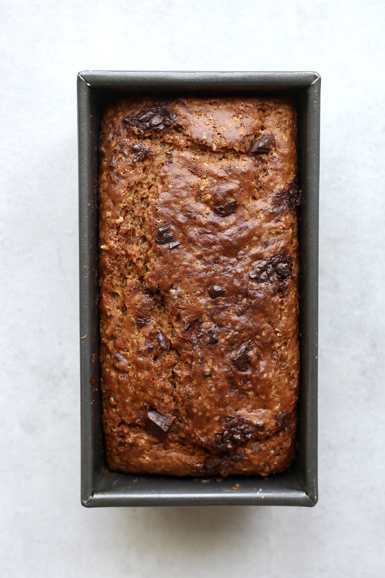 Golden brown pumpkin bread with chocolate chips on top in a loaf pan. 