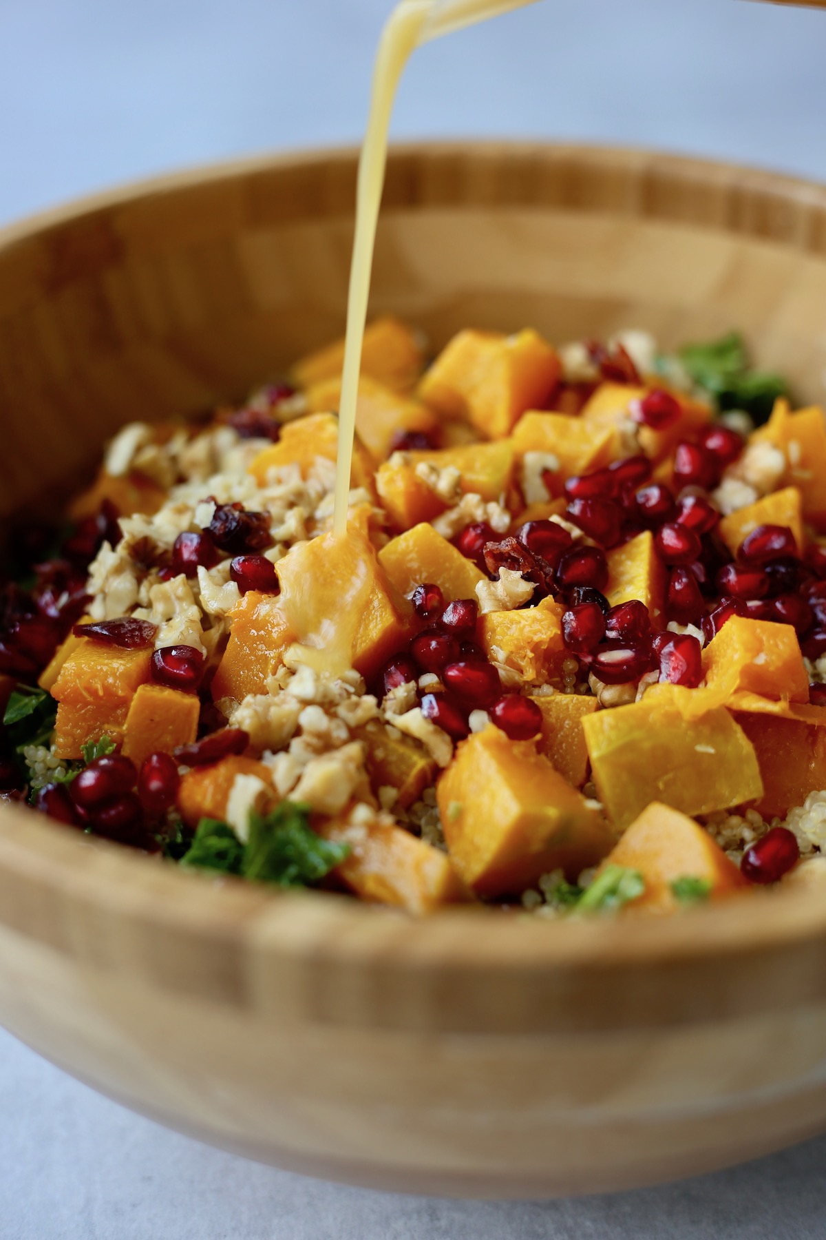 Zesty orange dressing being poured overtop of a quinoa, kale and squash salad