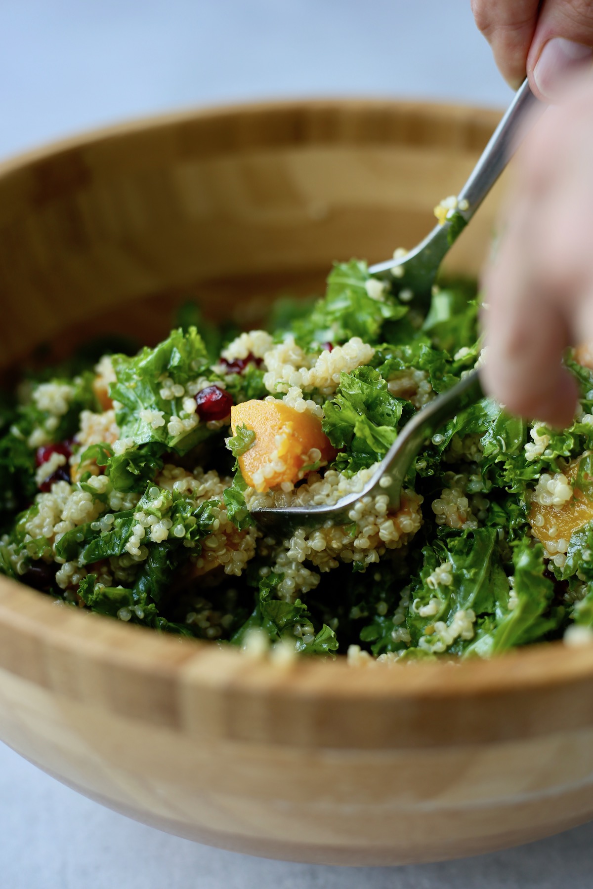 Quinoa, kale and squash salad being scooped out of a wooden bowl with two spoons