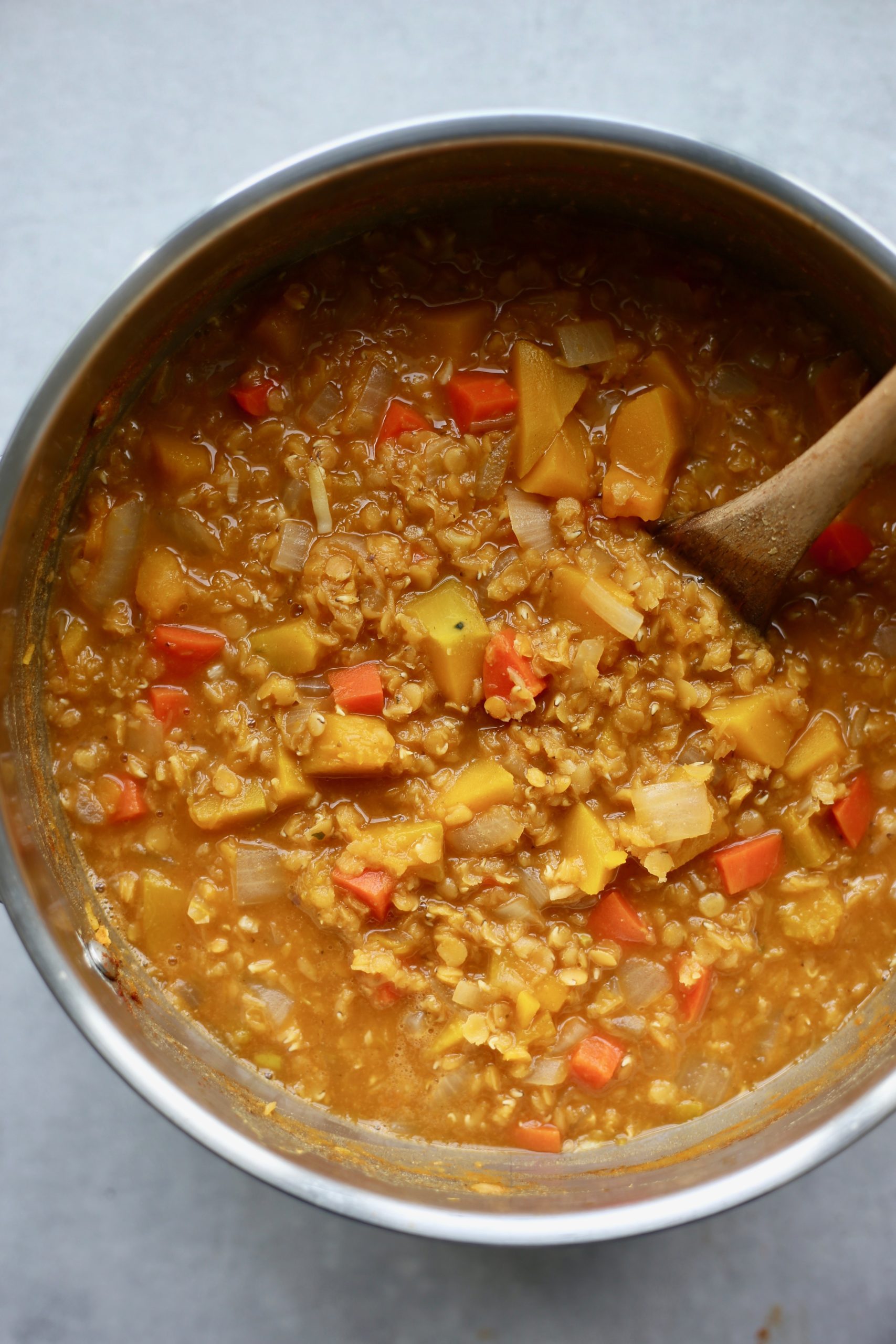 An overhead shot of chunky red lentil and pumpkin soup being stirred with a wooden spoon.