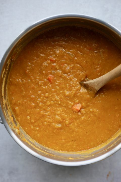 Creamy red lentil and pumpkin soup being stirred in a pot