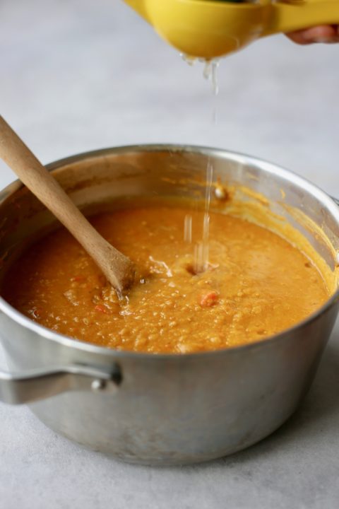 Lemon juice being squeezed into a pot of red lentil pumpkin soup