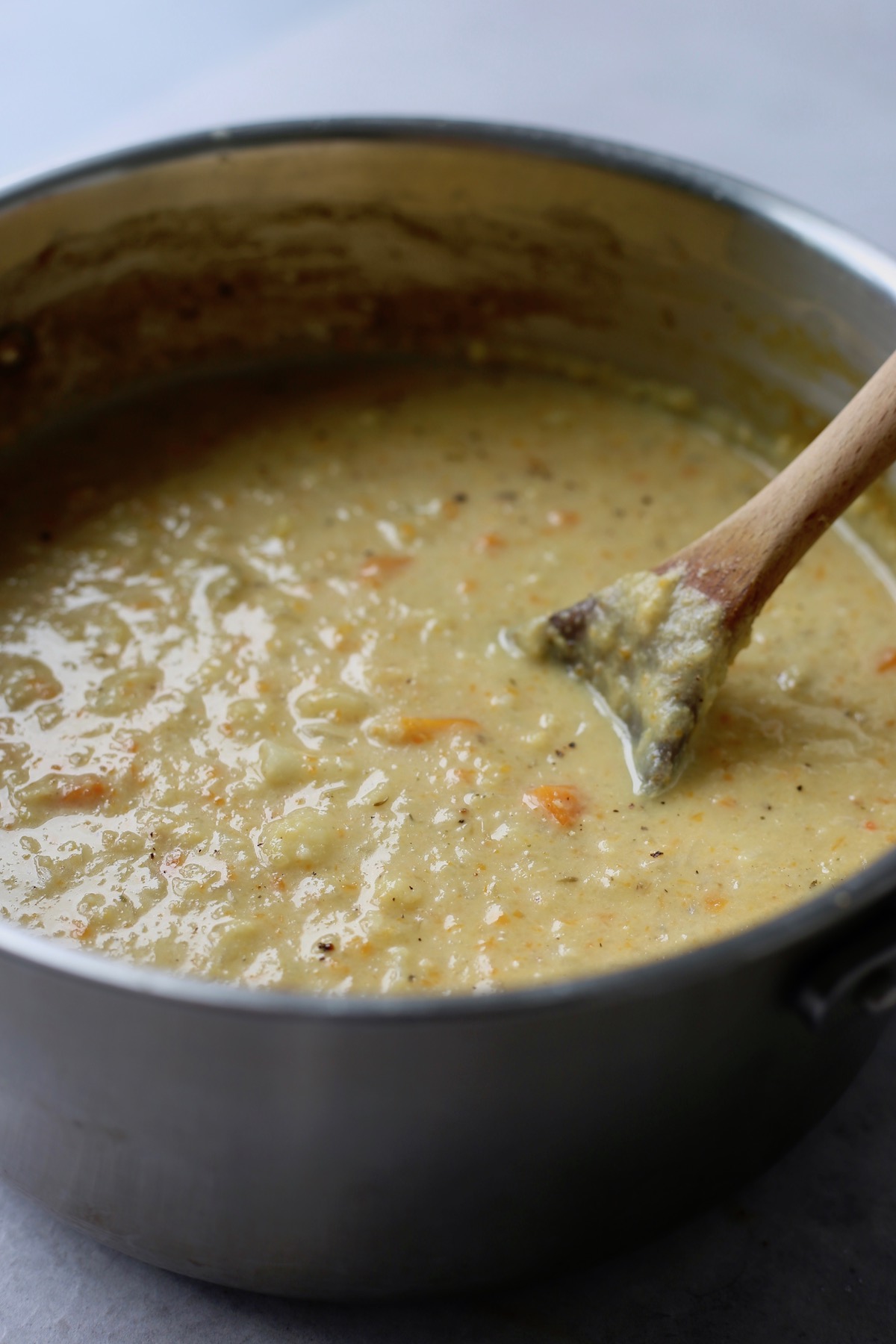 A pot of vegan, roasted cauliflower chowder being stirred with a wooden spoon