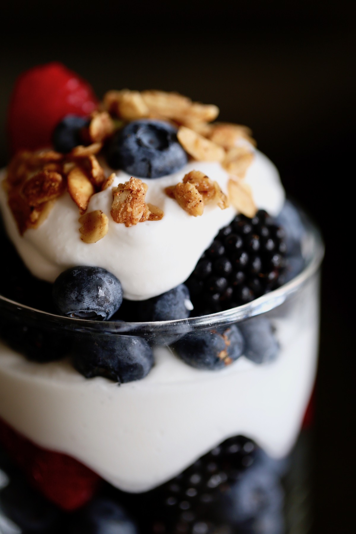 a close-up of granola and coconut milk whipped cream topping fresh berries in a glass jar