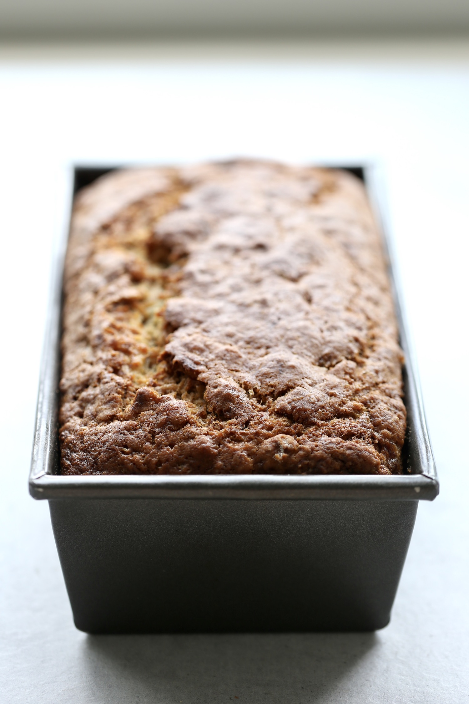 A back lit photo of golden brown banana bread in a loaf pan. 