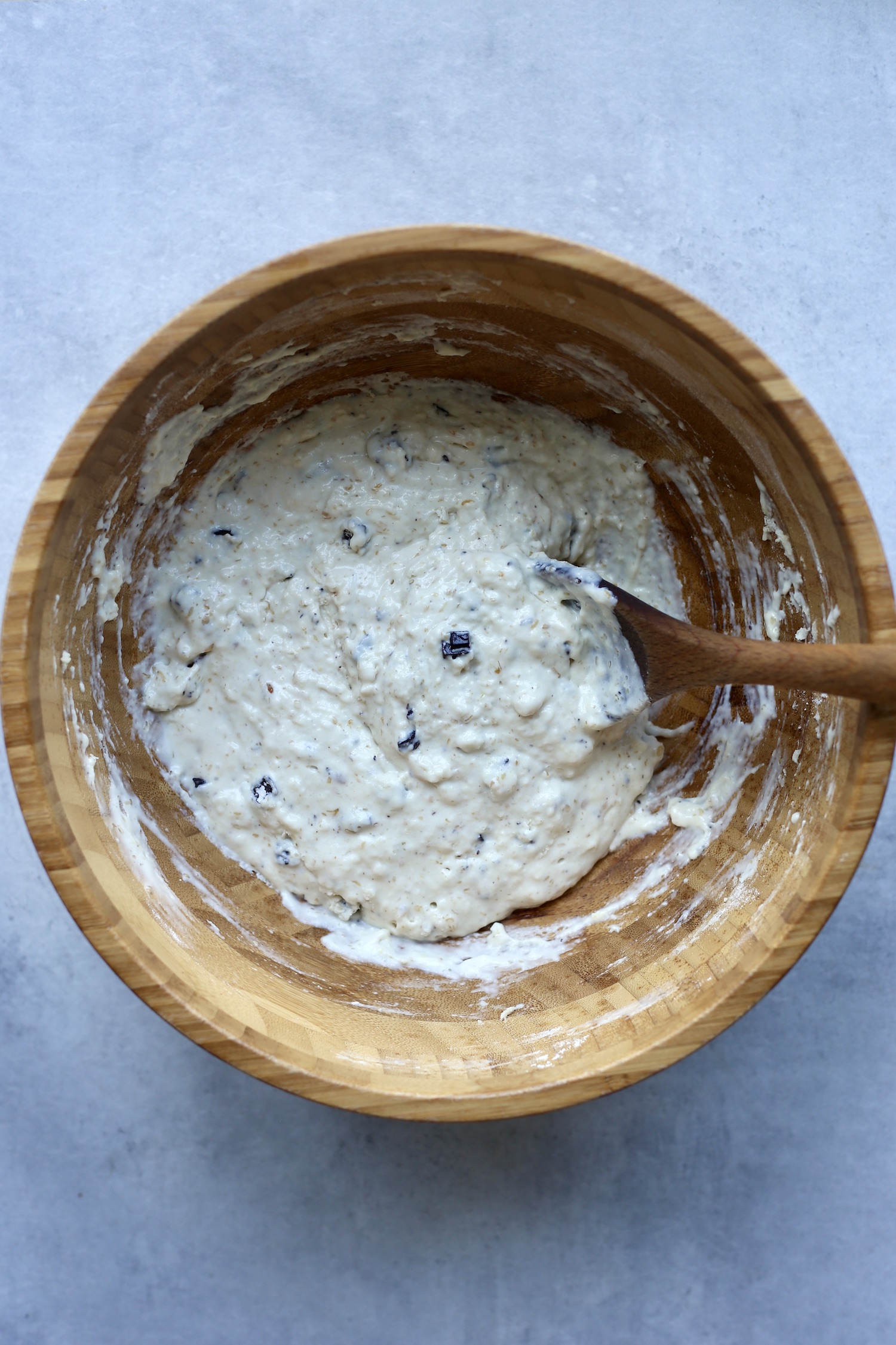 A wooden spoon gently stirring flour and chocolate chips into sourdough muffin batter.