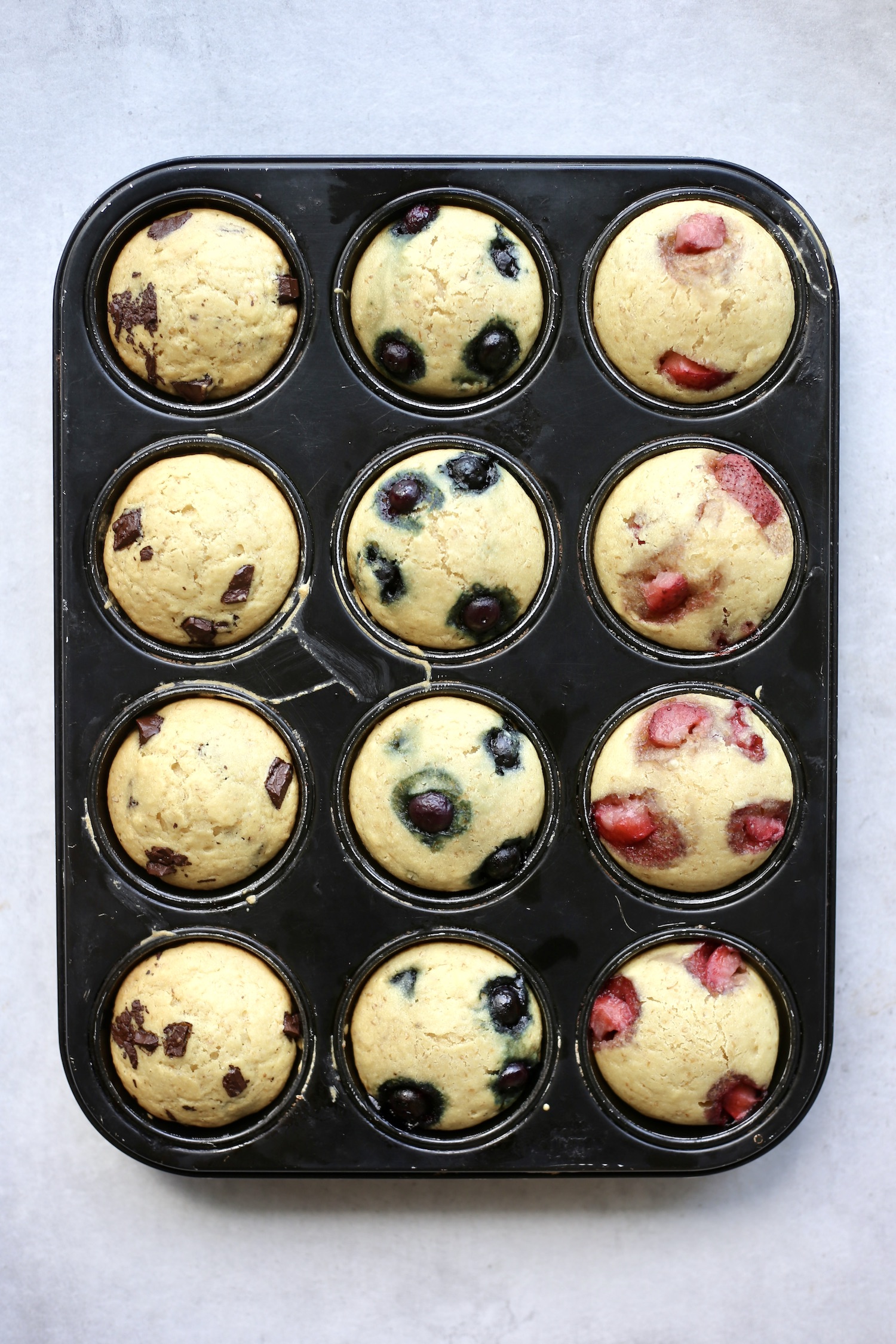 Chocolate chip, blueberry and strawberry sourdough muffins cooling in a muffin tin. 